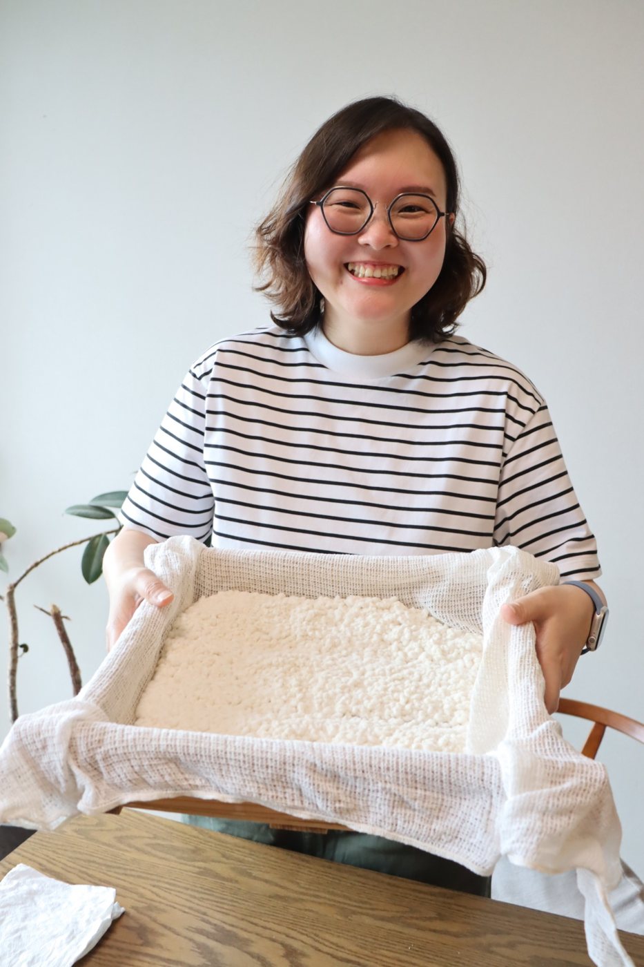 蒸した米に麹をつけた箱を持つ Joy さん