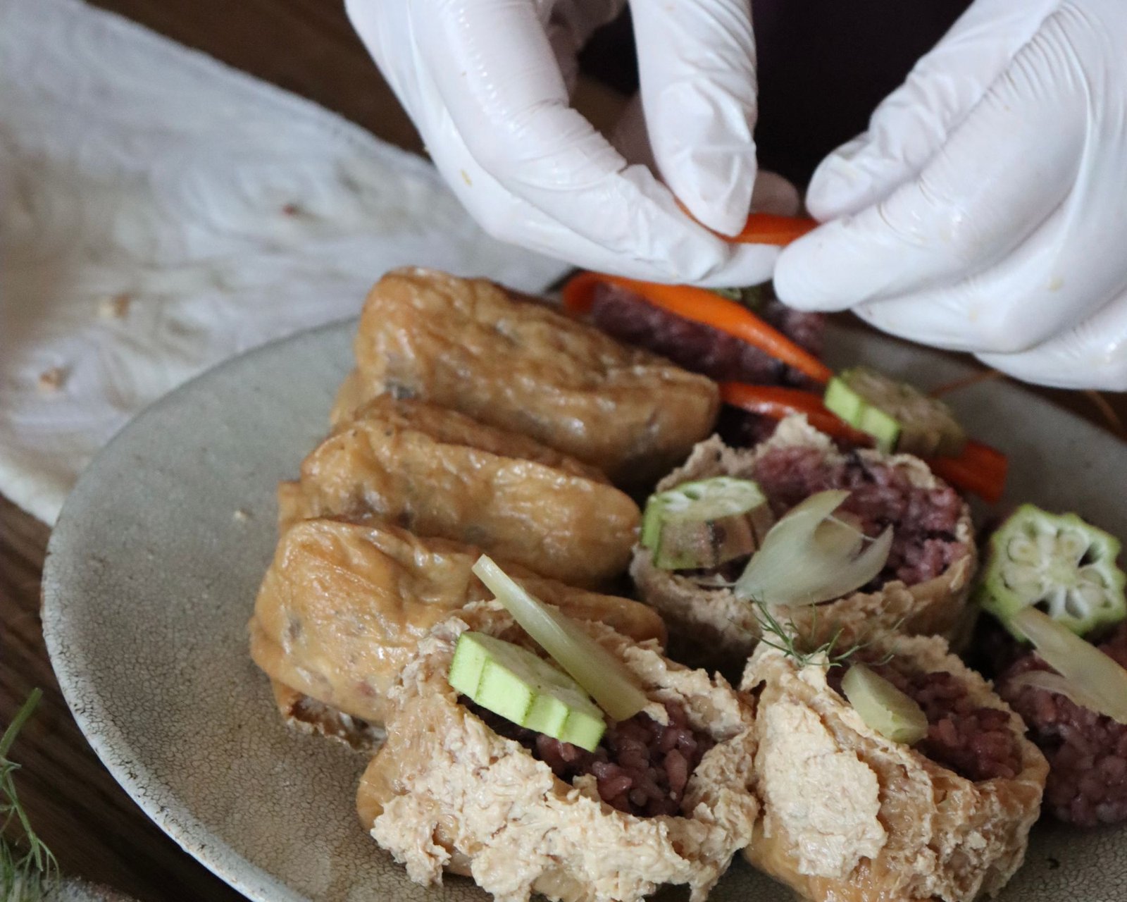 Vegetable inari sushi with red rice, okra and carrot being finished by hand on a ceramic plate