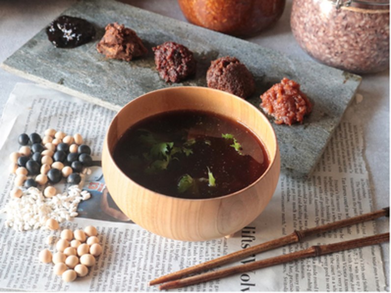 Miso soup in a wooden bowl, with soybeans, rice koji and several kinds of miso on the table