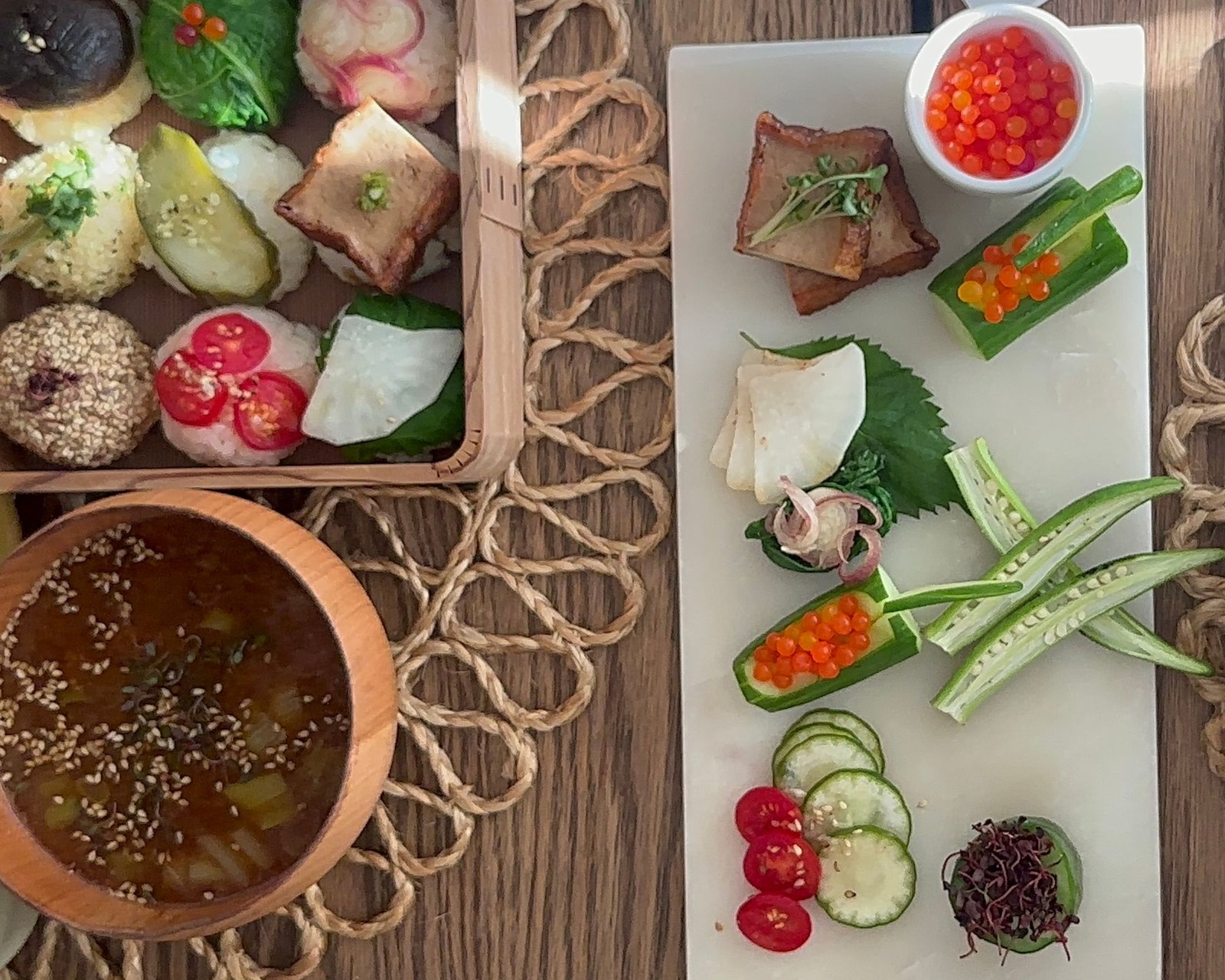 Vegetable temari sushi, miso soup with sesame and a plate of seasonal vegetables on a wooden table